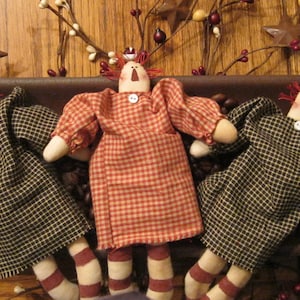 May include: Three handmade rag dolls with red hair and button eyes. The dolls are wearing plaid and gingham dresses. The dolls are sitting in a brown bowl filled with coffee beans.