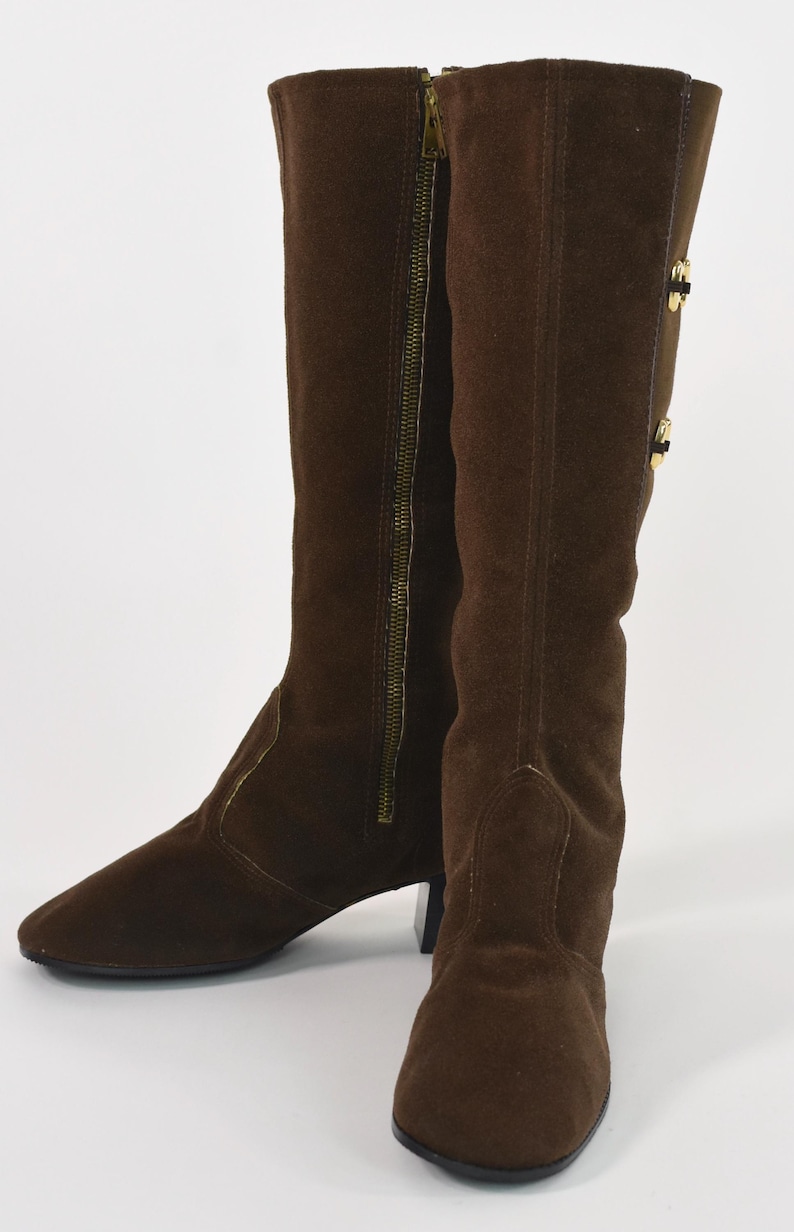 Puede incluir: Un par de botas altas de ante marr&oacute;n. Las botas tienen punta, un tac&oacute;n peque&ntilde;o y una cremallera dorada en el lateral. Acentos dorados en el lateral de la bota.