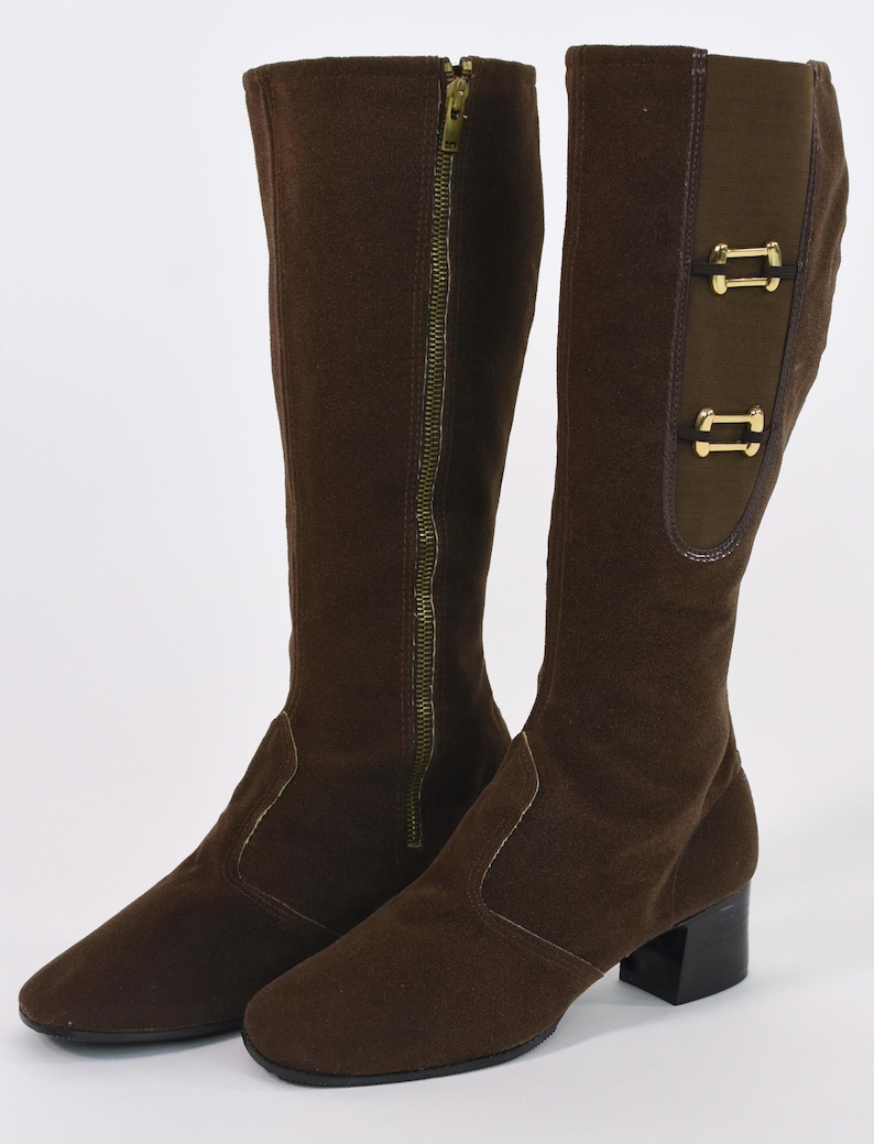 Puede incluir: Un par de botas marrones hasta la rodilla. Una bota tiene una cremallera dorada de largo completo. La otra bota tiene dos hebillas decorativas doradas. Las botas tienen un tac&oacute;n peque&ntilde;o y negro y una puntera en punta.