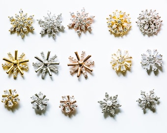 May include: Assortment of snowflake-shaped charms with crystal embellishments in gold, silver, and rose gold finishes. The charms are perfect for jewelry making, scrapbooking, and other craft projects.
