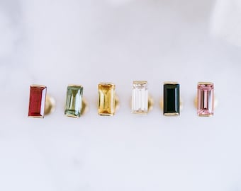 May include: Six gold stud earrings with different coloured gemstones. The gemstones are red, green, yellow, clear, black, and pink.