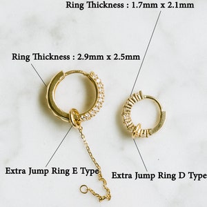 Peut inclure: Deux boucles d'oreilles cr&eacute;oles en or reli&eacute;es par une cha&icirc;ne. La plus grande cr&eacute;ole est orn&eacute;e d'une rang&eacute;e de petites pierres claires sur le bord. La plus petite cr&eacute;ole est orn&eacute;e d'une rang&eacute;e de petites pierres rectangulaires sur le bord. La cha&icirc;ne se termine par un petit anneau de jonction. Le texte "Ring Thickness: 1.7mm x 2.1mm" et "Ring Thickness: 2.9mm x 2.5mm" est visible au-dessus des cr&eacute;oles. Le texte "Extra Jump Ring E Type" et "Extra Jump Ring D Type" est visible en dessous des cr&eacute;oles.