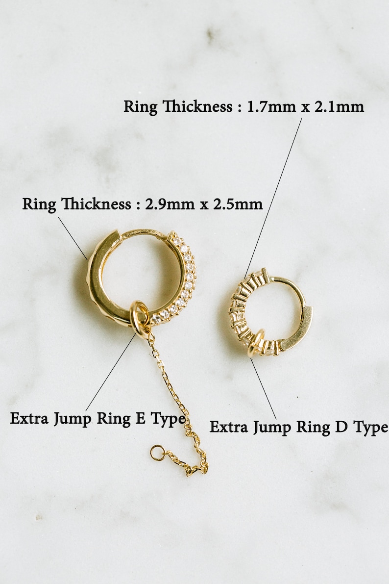 Peut inclure: Deux boucles d'oreilles cr&eacute;oles en or reli&eacute;es par une cha&icirc;ne. La plus grande cr&eacute;ole est orn&eacute;e d'une rang&eacute;e de petites pierres claires sur le bord. La plus petite cr&eacute;ole est orn&eacute;e d'une rang&eacute;e de petites pierres rectangulaires sur le bord. La cha&icirc;ne se termine par un petit anneau de jonction. Le texte "Ring Thickness: 1.7mm x 2.1mm" et "Ring Thickness: 2.9mm x 2.5mm" est visible au-dessus des cr&eacute;oles. Le texte "Extra Jump Ring E Type" et "Extra Jump Ring D Type" est visible en dessous des cr&eacute;oles.