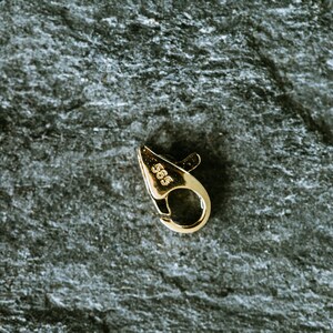 May include: A gold-toned metal clasp with a spring-loaded closure. The clasp is marked with the number "585", indicating it is made of 14 karat gold.