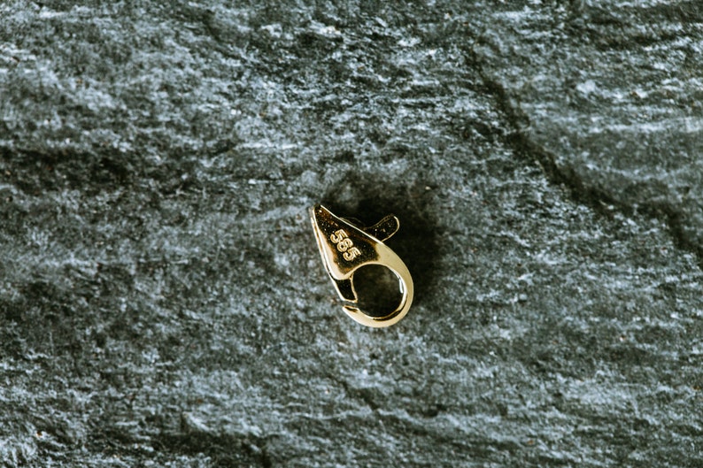 May include: A gold-toned metal clasp with a spring-loaded closure. The clasp is marked with the number "585", indicating it is made of 14 karat gold.