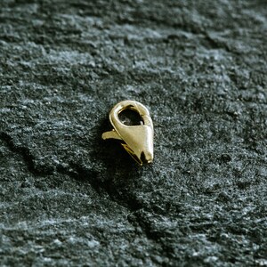 May include: A gold-toned metal clasp for jewelry making. The clasp is a lobster claw style with a spring-loaded opening.