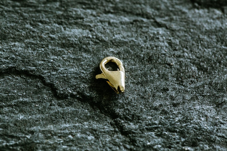 May include: A gold-toned metal clasp for jewelry making. The clasp is a lobster claw style with a spring-loaded opening.