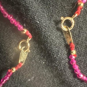 Pu&ograve; includere: Primo piano di una collana rossa e dorata con una chiusura che recita "585".