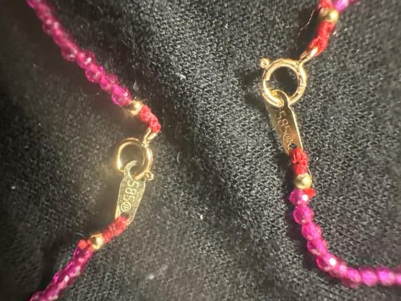Pu&ograve; includere: Primo piano di una collana rossa e dorata con una chiusura che recita "585".