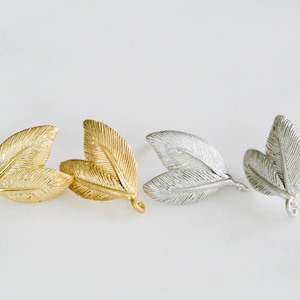 May include: Two pairs of leaf-shaped earrings, one pair in gold and one pair in silver. The earrings are made of metal and have a simple, elegant design.