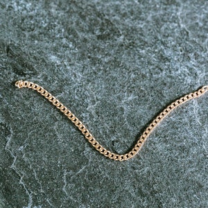 May include: A gold chain bracelet on a gray textured background.