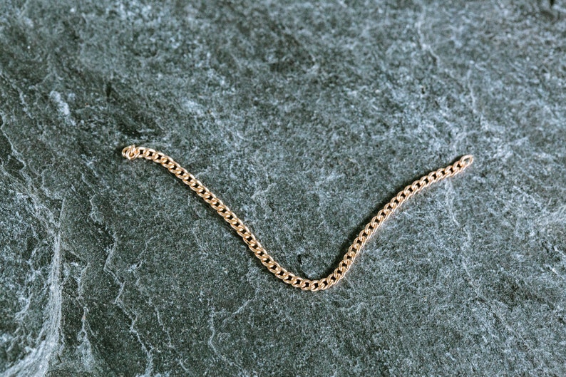 May include: A gold chain bracelet on a gray textured background.