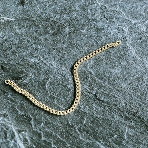 May include: A gold chain necklace on a gray textured background.