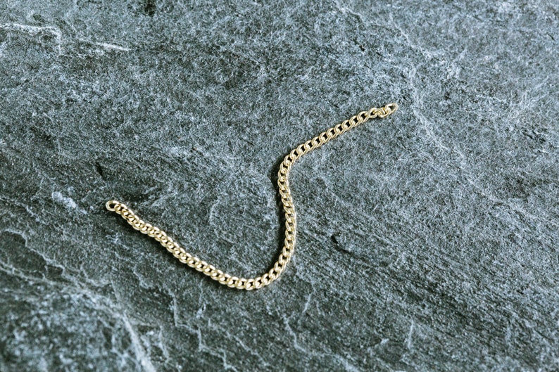 May include: A gold chain necklace on a gray textured background.