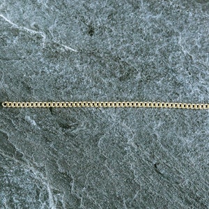 May include: A gold chain necklace on a gray textured background.