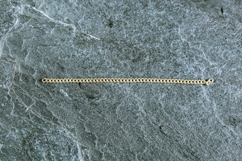 May include: A gold chain necklace on a gray textured background.