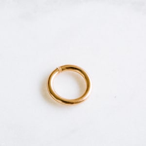 Peut inclure: Un anneau de saut en m&eacute;tal de couleur or est pr&eacute;sent&eacute; sur un fond blanc. L'anneau est ouvert et pr&ecirc;t &agrave; &ecirc;tre utilis&eacute; pour la fabrication de bijoux.