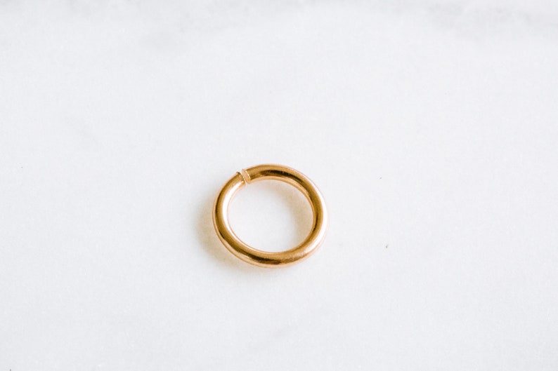 Peut inclure: Un anneau de saut en m&eacute;tal de couleur or est pr&eacute;sent&eacute; sur un fond blanc. L'anneau est ouvert et pr&ecirc;t &agrave; &ecirc;tre utilis&eacute; pour la fabrication de bijoux.