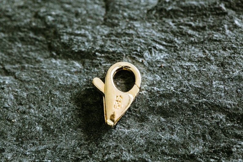 May include: A gold-toned metal clasp with a spring-loaded closure. The clasp is marked with "585", indicating it is made of 14 karat gold.