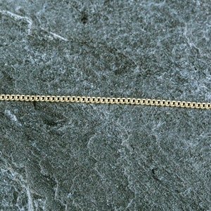 May include: A gold chain necklace on a gray textured surface.