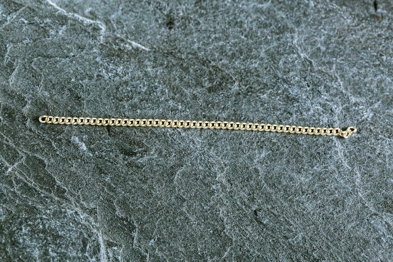 May include: A gold chain necklace on a gray textured surface.