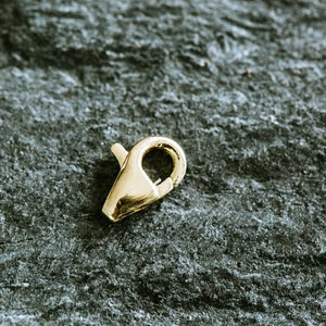May include: A gold-toned metal clasp for jewelry making. The clasp is a simple, functional design with a spring-loaded mechanism.