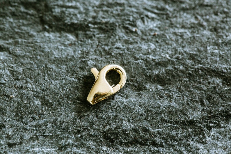 May include: A gold-toned metal clasp for jewelry making. The clasp is a simple, functional design with a spring-loaded mechanism.