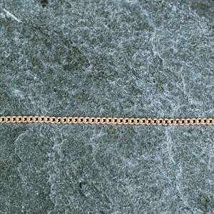 May include: A gold chain necklace on a gray textured background.
