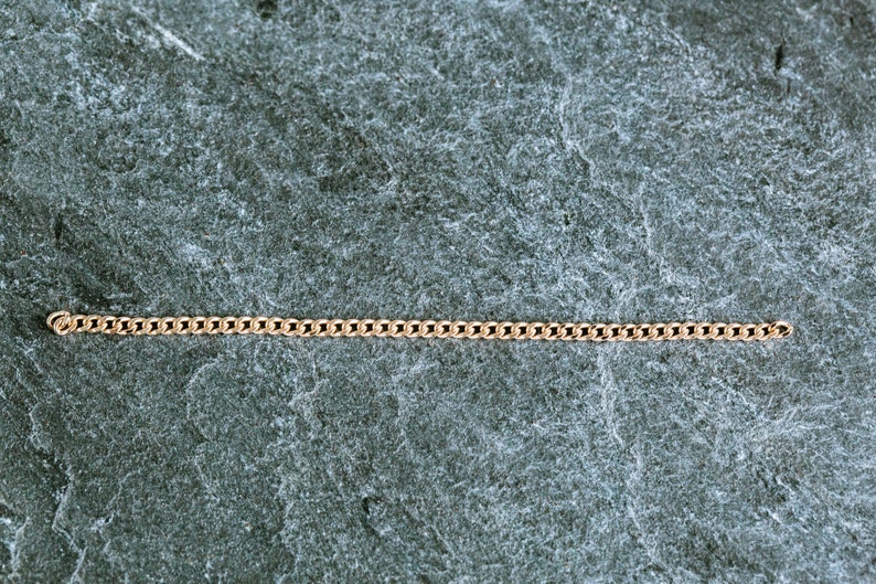 May include: A gold chain necklace on a gray textured background.