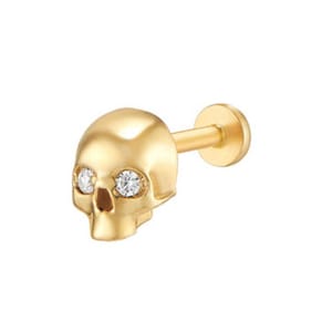 May include: A gold-toned flat back stud earring featuring a polished skull design. The skull has two small, clear, round-cut stones set into the eye sockets. The earring includes a straight post and a circular flat backing for secure placement.