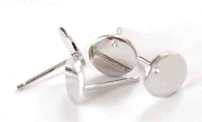 May include: Three silver earring blanks with a round, flat base and a post for attaching earrings. The blanks are designed for crafting and customizing.