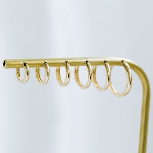 以下が含まれることがあります： 6つの異なるサイズの金色のフープイヤリングが付いた、金色の金属製ディスプレイスタンドです。