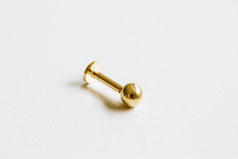 May include: A gold-colored barbell with a small ball on one end and a flat disc on the other end.