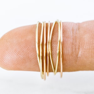 Peut inclure: Un ensemble de cinq fines bagues dorées empilées sur un doigt. Les bagues sont de tailles différentes et ont une texture martelée.