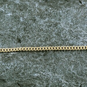 May include: A gold chain necklace on a gray textured background.