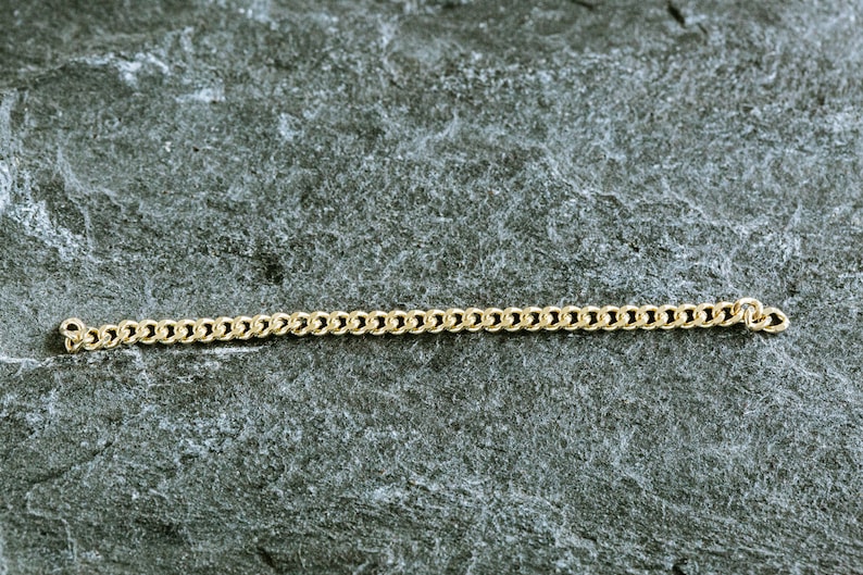 May include: A gold chain necklace on a gray textured background.