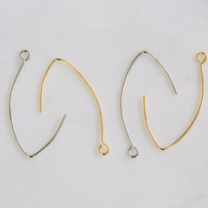 Op de afbeelding: Drie oorhaken, twee goud en één zilver, liggen op een wit oppervlak. De haken hebben allemaal de vorm van een traan.