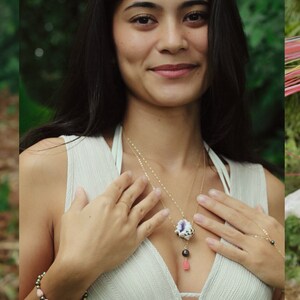 May include: A woman wearing a white sleeveless top with a gold chain necklace featuring a shell pendant and a pink coral bead. She is also wearing a gold ring on her finger and a gold bracelet with black beads on her wrist.