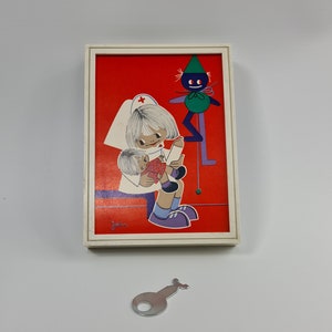 May include: A white framed picture with a red background. The picture shows a girl in a white nurse's uniform holding a doll. A green and purple puppet is in the background. The picture is signed "Josie".