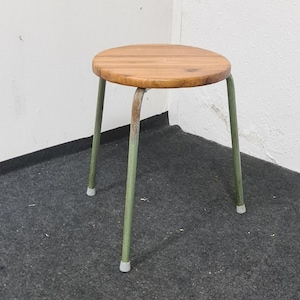Puede incluir: Un pequeño taburete redondo de madera con estructura de metal verde. El taburete tiene patas de plástico blanco.