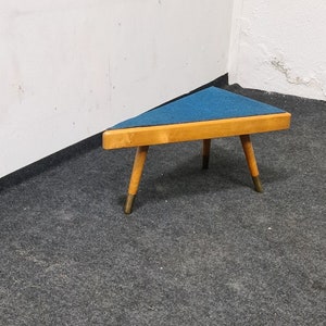 May include: A triangular wooden stool with a blue fabric top and gold-coloured legs.