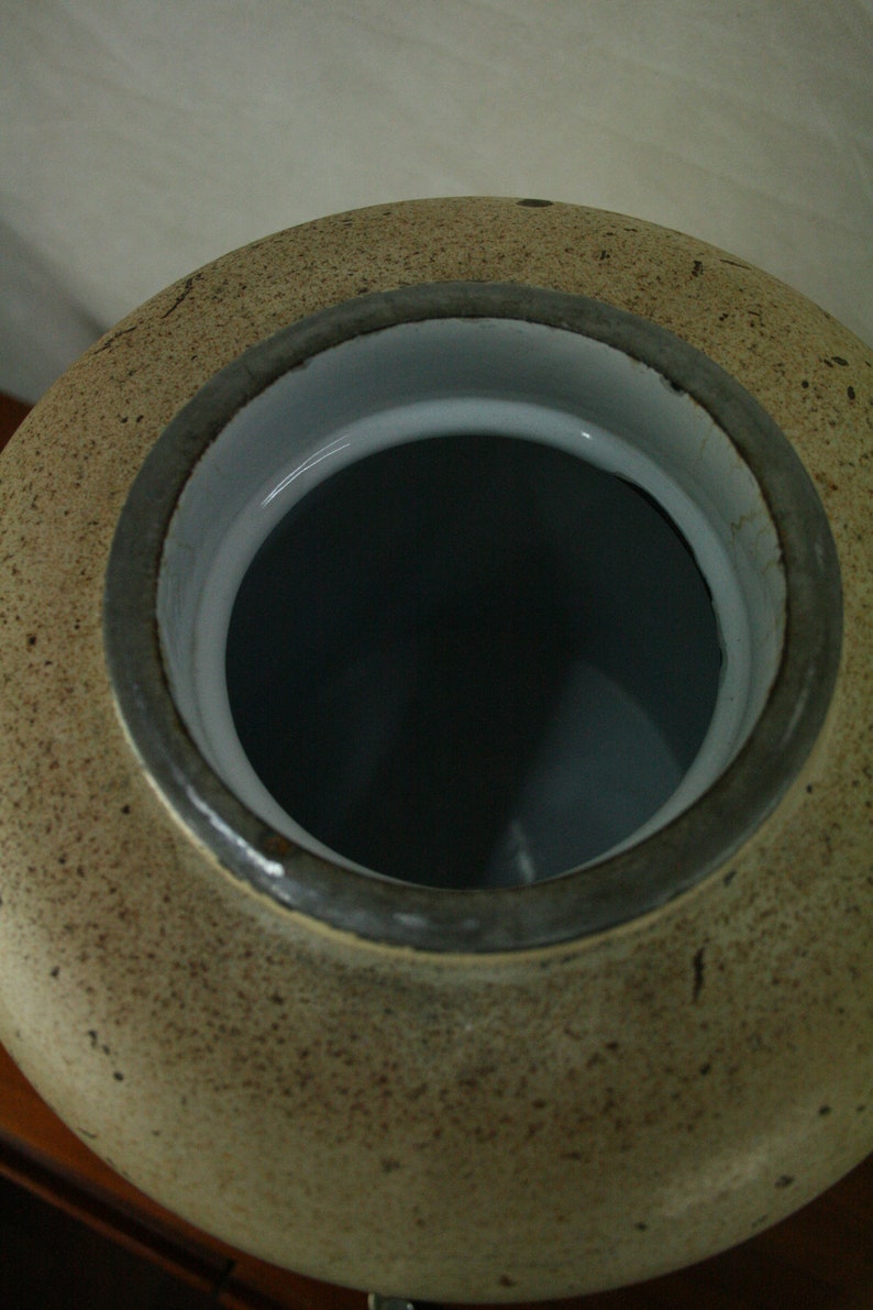 May include: A large, round, ceramic jar with a speckled brown glaze. The jar has a wide opening with a white porcelain rim and a dark gray metal band.