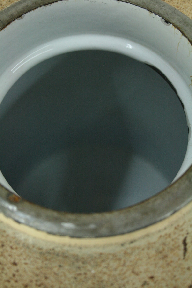 May include: A large, round, ceramic jar with a wide opening. The jar is brown with a light brown glaze and has a white interior.
