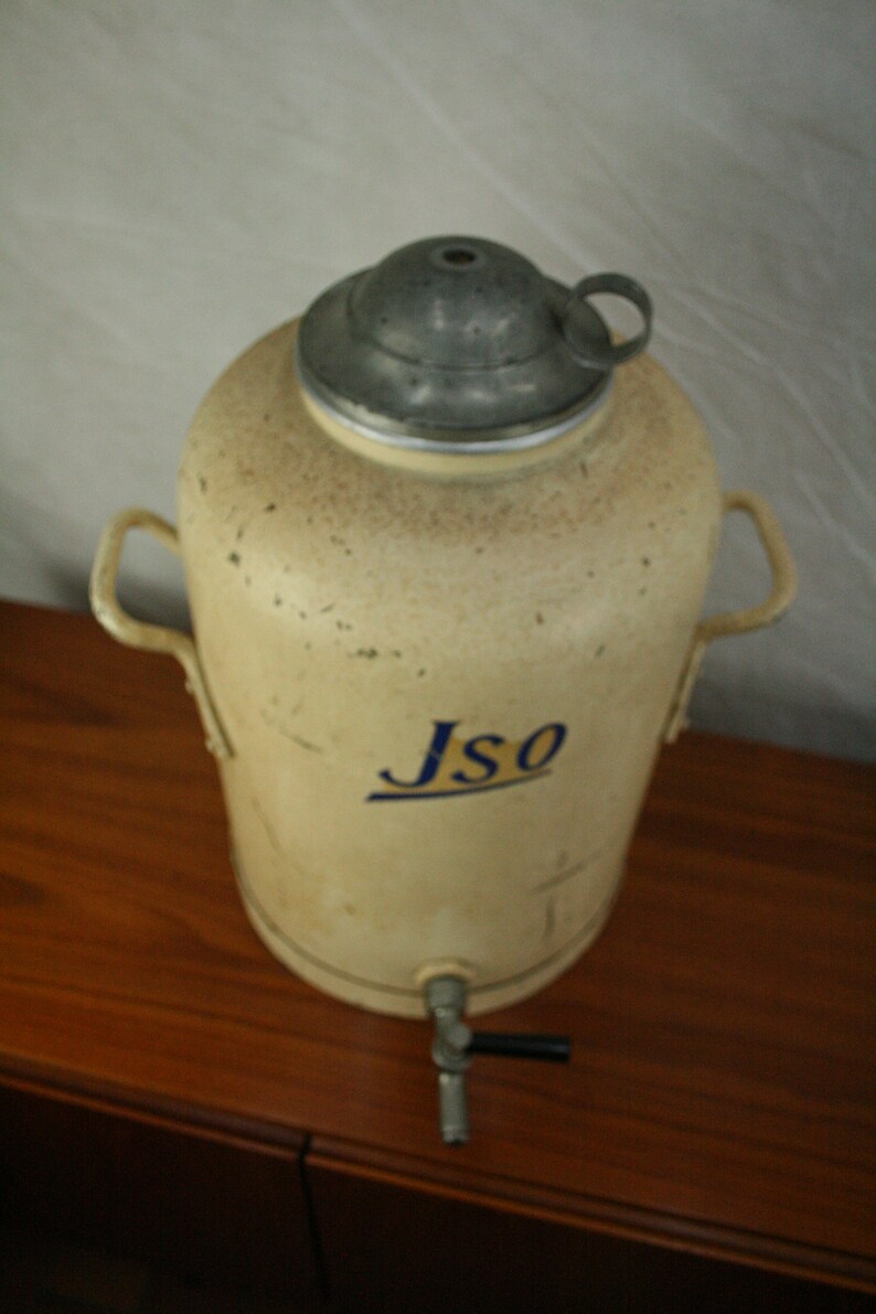 May include: A vintage, cream-colored metal water dispenser with a silver lid and a blue and yellow "Jso" logo. The dispenser has two handles and a spigot.