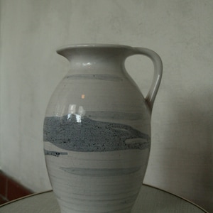 May include: A white ceramic vase with a gray and white marbled design. The vase has a wide mouth and a handle.