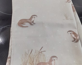 Tea towel/ drying cloth in an otter design on a stone coloured background.