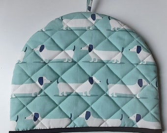 A stylish padded tea cosy in organic cotton in a seafoam blue dachshund dog design, lined in white cotton and trimmed in black tape.