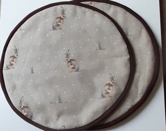 A pair of aga covers in a Hartley hare design on  a beige background, insulated and lined in cream cotton , bound in dark brown binding..