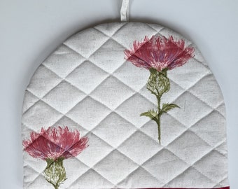 A stylish padded tea cosy in organic cotton in a pink thistle design, lined in white cotton and trimmed in red tape.