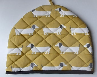 A stylish padded tea cosy in organic cotton in a yellow ochre dachshund dog design, lined in white cotton and trimmed with  black tape.